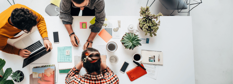 Blick von oben auf eine Arbeitsgruppe mit drei Personen an einem Schreibtisch